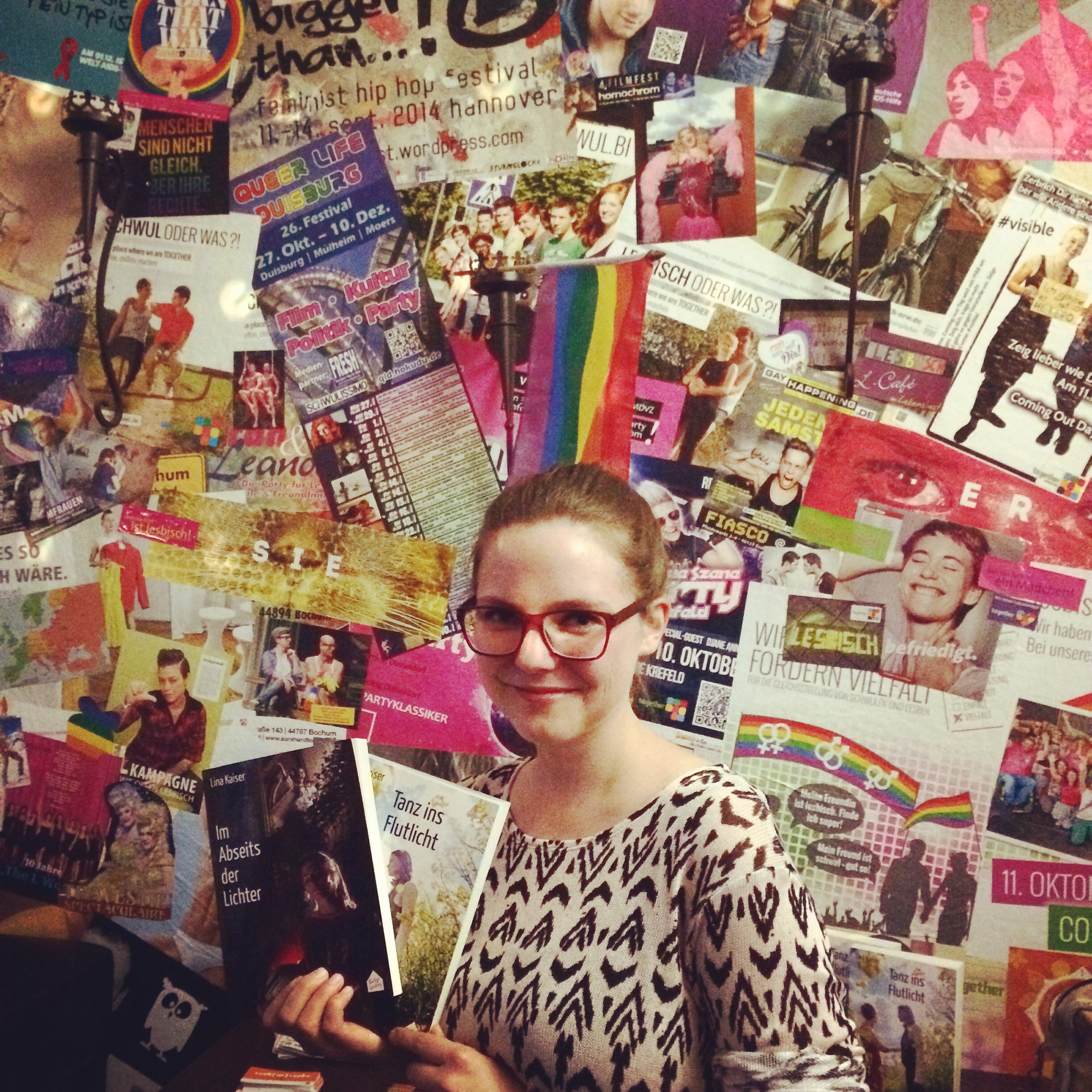 Lina Kaiser bei einer Lesung im together Mülheim vor einer LGBT-Bilderwand